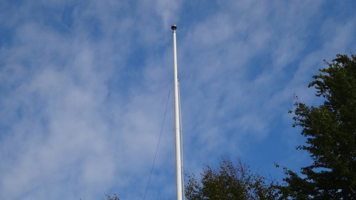 En 11 meters flaggstång mot en molnig himmel, med en nyligen installerad flagglina synlig längs stångens längd.