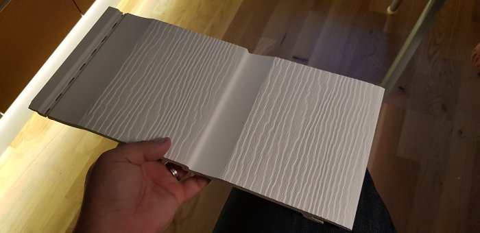 Hand håller upp ett öppet prov av Sverigepanelen med synligt plastliknande textur.