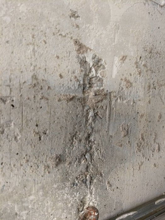 Vägg med ojämnheter och rester av material efter borttagning av kakelplattor, möjlig asbestkontaminering.