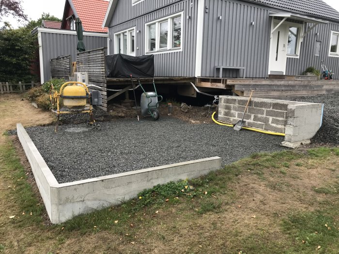 Bild av grunden till ett hus med lecamur, grus och byggmaterial framför, under renovering.