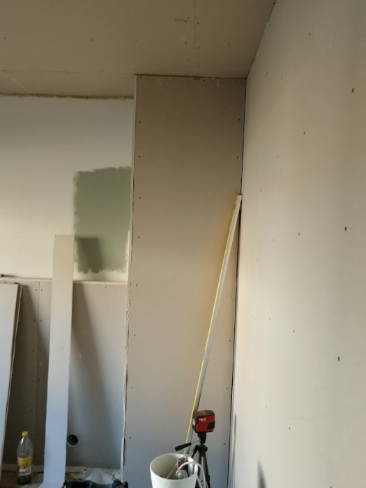 Nyuppbyggd innergipsvägg i renoveringsprocess med synlig mätlaser och spackel.