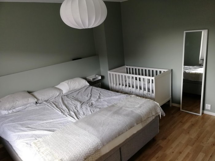 Nyrenoverat sovrum med dubbelsäng, spjälsäng, sänggavel och stående spegel.