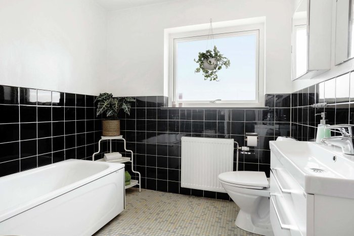 Vintage badrum med svart kakel halvvägs upp på väggarna och små gula golvkakel, toalett, badkar och handfat.