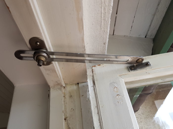 Äldre dörrbroms monterad på vit dörrkarm med justerbar metallarm och fästelement.