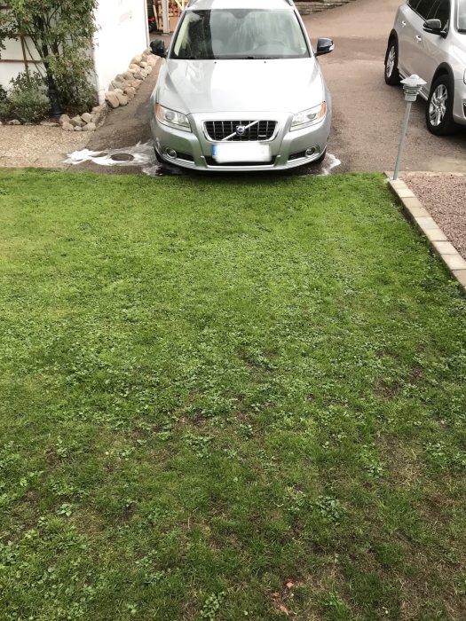 En bil framför en gräsmatta vid en uppfart, potentiellt risk för skador vid parkering på gräset.