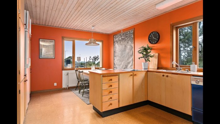 Retro kök med orange väggar, träskåp och vitvaror, parkettgolv, fönster och matplats.