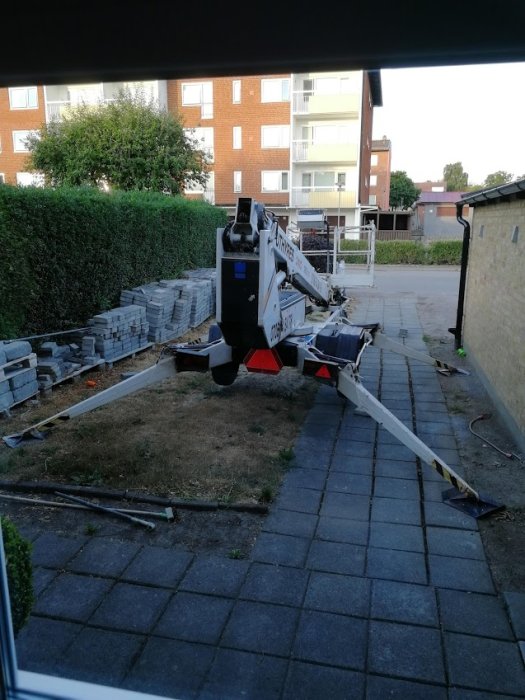Skylift parkerad på en bostads bakgård omgiven av tegelstenar och en häck.