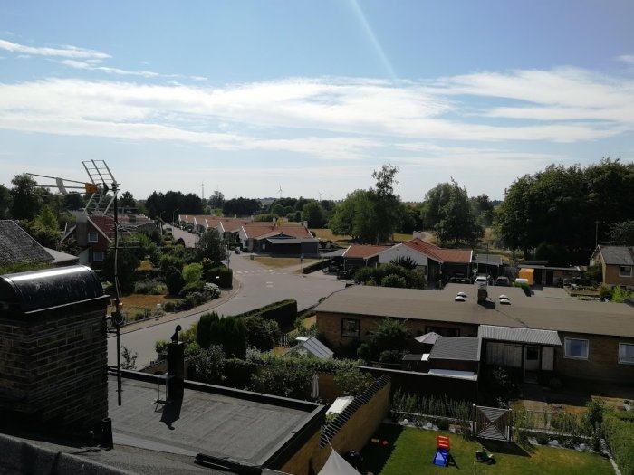 Vy över en förort med hus och trädgårdar från ett skylift, soligt väder.