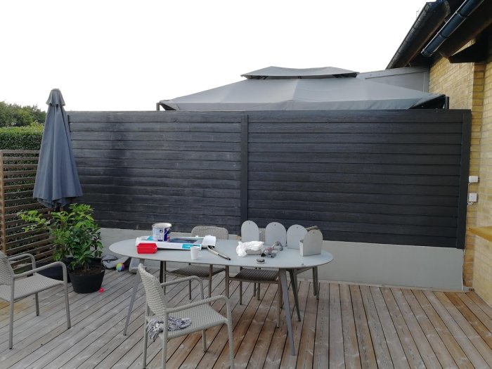 Terrass med staket målat i ny nyans och uteplats med bord, stolar och öppen parasoll.