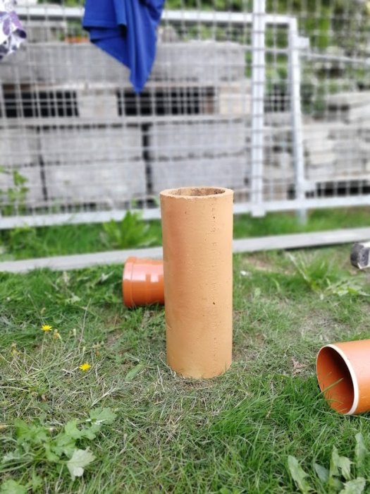 Rengjort tegelrör står i gräset med andra rör och en stengabionkorg i bakgrunden, ett projekt för dränering av framsidan.