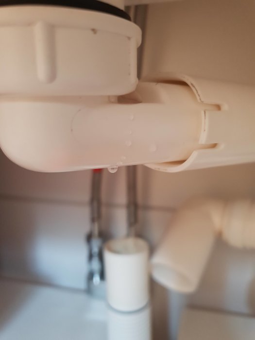 Vattenläckage vid en vit avloppskoppling under handfatet med droppar som bildas.