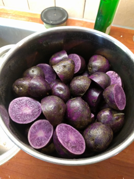Lila "Salad Blue" potatisar i en kastrull, några skurna och visa den mörklila insidan.