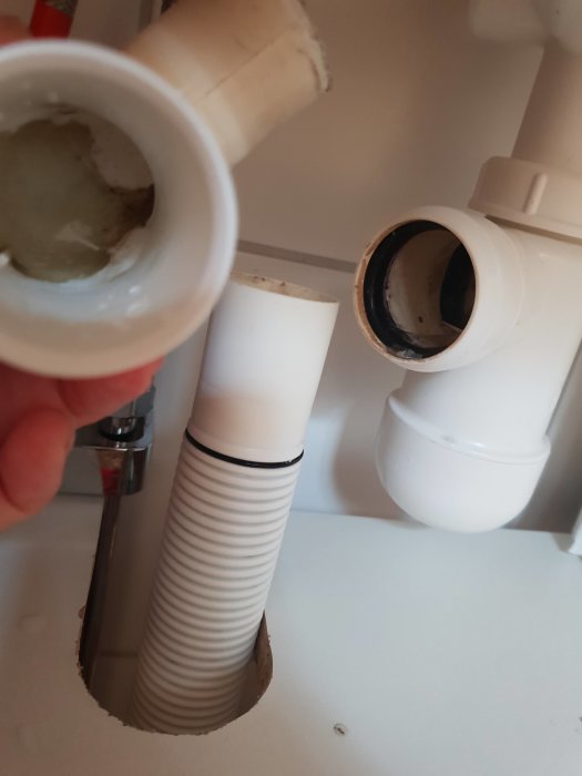 Närbild på avlägsnad avloppskrok och ett röravsnitt med tätning i ett köksskåp.