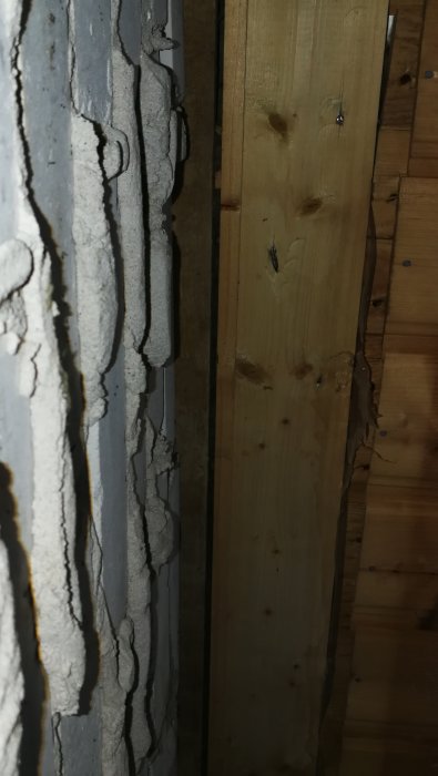 Hammarband i ljusare trä vid en innervägg, mörkare ohyvlat trä mot tegelvägg, glipa leder till vind.