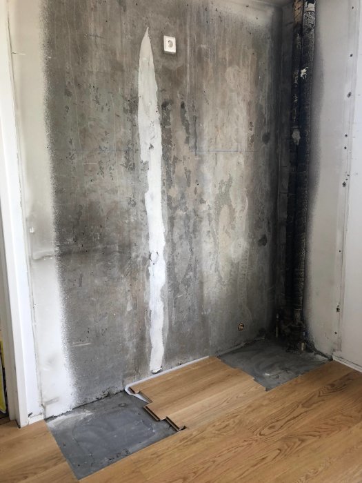 Delvis demonterat köksgolv som visar underliggande betong och vägg, med några plattor av vad som ser ut att vara parkett.