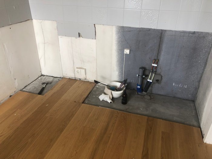 Ej färdigt köksgolv med brädor på betongunderlag, verktyg och VVS-installationer synliga.