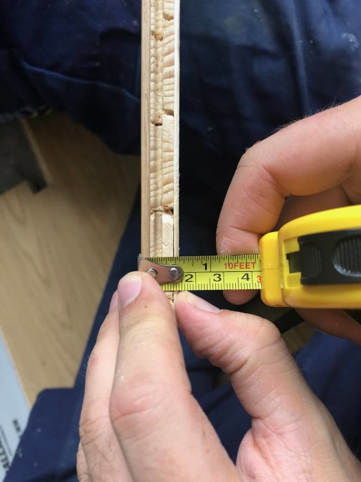 Person mäter tjockleken på ett trägolvplank med en gul tumstock, potentiellt parkett, för renovering.