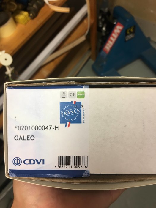 En hand som håller en förpackning av CDVI Galeo med informationsetiketter.