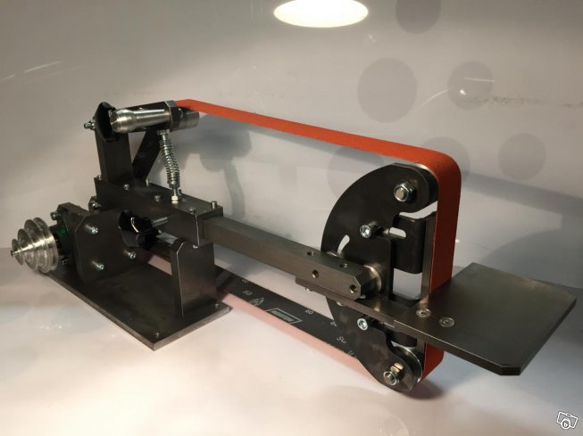 Bild på en Håkansson slipmaskin för knivtillverkning med orange slipband, svart metallkonstruktion och slipstöd.
