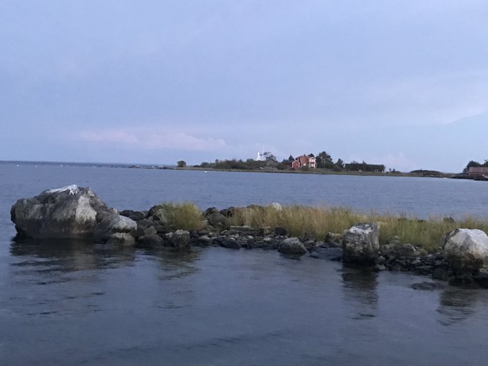 Sjöutsikt med stenar i förgrunden, ö i mitten och skeppet TRANSLONTANO på ankare i bakgrunden.