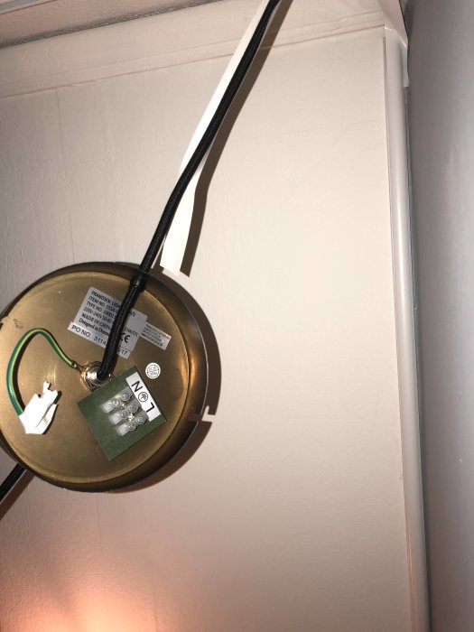 Takmonterad lampdosa med tre utstickande kablar, blå, brun och gul/grön, längs en vit vägg.