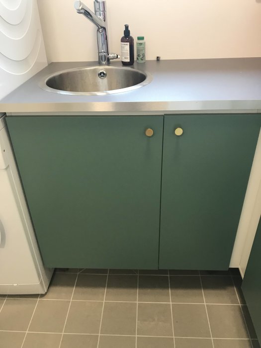 Tvättstuga med ommålade gröna skåpluckor och nya runda knoppar, integrerad diskho och tvättbänk.