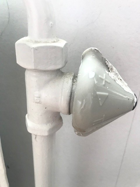Gammal vit TA-ventil från 1964 monterad på ett radiatorrör, behov av utbyte till en termostatventil.