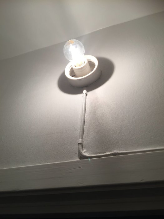 Väggmonterad lampa med en synlig, målad kabelföring fastspikad på dörrfoder.