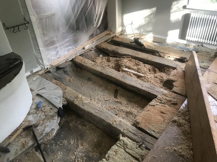 Upprivet gammalt plankgolv med synliga bjälkar och gammal isolering, renoveringsarbete pågår.