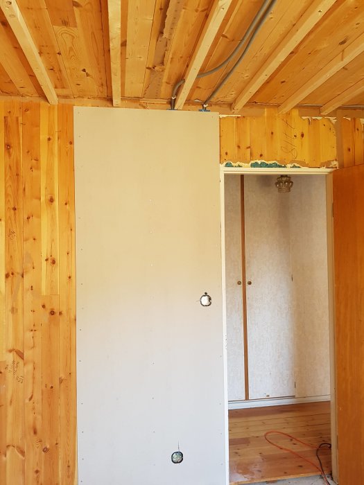 Renoveringsarbete i rum med synliga träreglar i tak och renoveringsgips på vägg, tom eluttag.