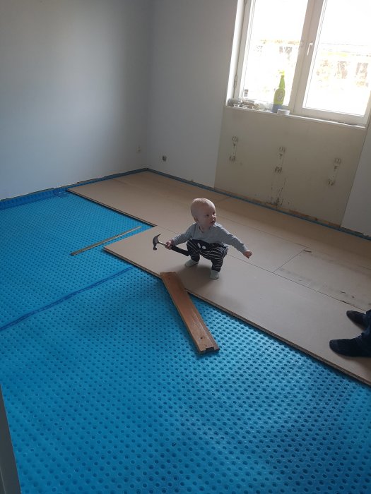 Renovering av sovrum med blå platonmatta på golvet och ett litet barn som sitter på golvet.