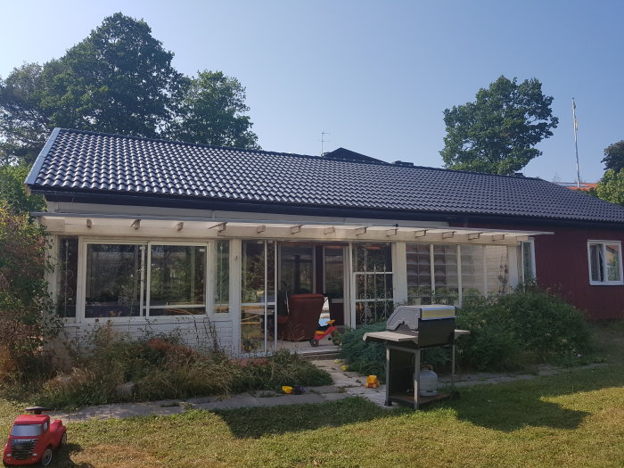Nyomlagt tak på ett enplanshus med trädgård och grill i förgrunden.
