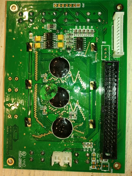 Grönt kretskort med olika elektroniska komponenter och anslutningar, inklusive kondensatorer och kontakter.