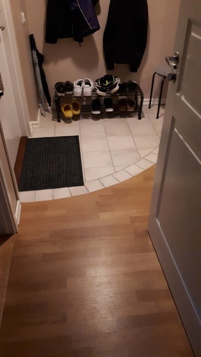 Entré med skohylla, skor, en hallmatta och jackor som hänger på krokar.
