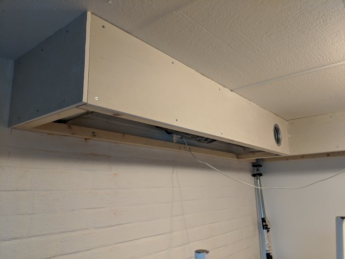 Inbyggd ventilationsbox i vägg med framträdande kablar och del av fläktsystemet synligt.