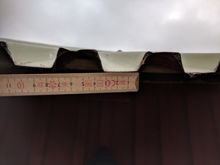 Närbild på takplåt med linjal som mäter profilens mått mot en skadad kant.