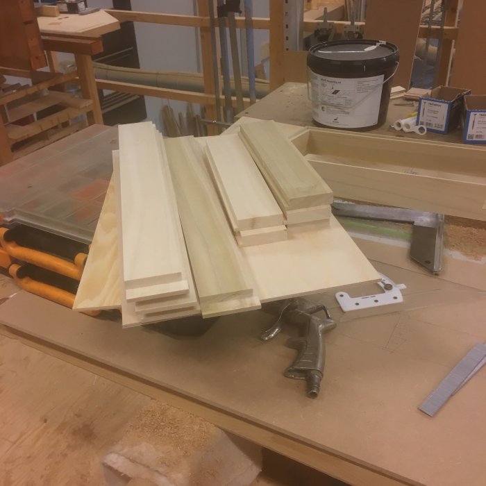 Trämaterial och verktyg på arbetsbänk i snickeri, under bearbetning för byggprojekt.