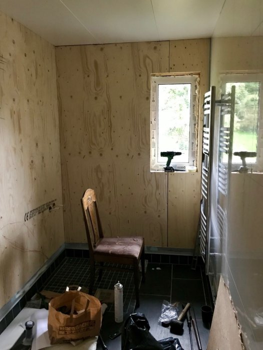 Badrum under renovering med plyfaskivor som väggar och verktyg och byggmaterial på golvet.