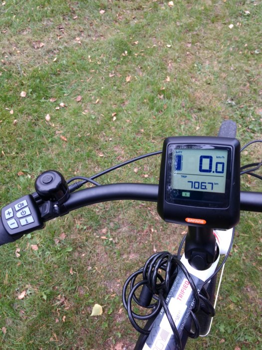 Styre på en elcykel med digital display som visar 706.7 km, knappsats och cykelvagnens lås.