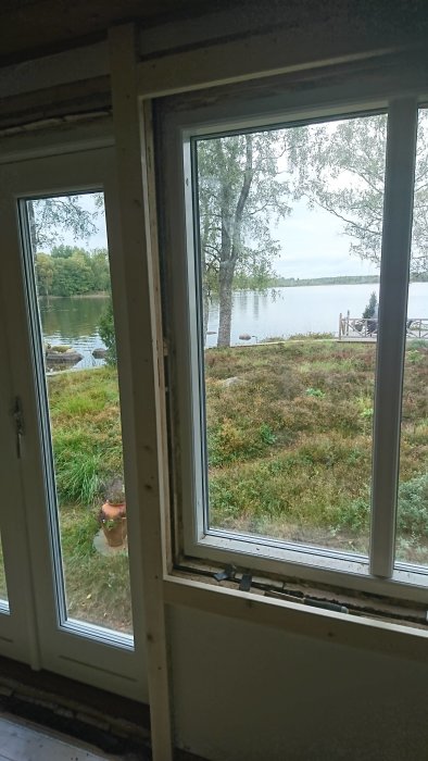 Utsikt genom nyligen installerat fönster och dörr mot en sjö och grönskande natur.