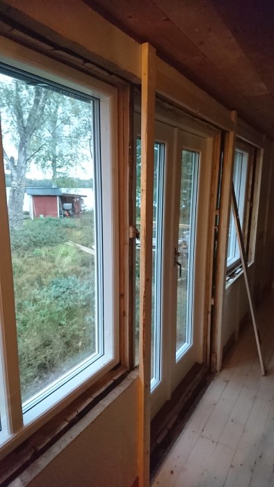 Nyinstallerade fönster med fönsterbleck och pardörr, inifån ett hus under renovering med utsikt över naturen.