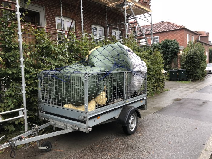 Släpvagn lastad med byggmaterial framför byggnadsställning vid husrenovering.