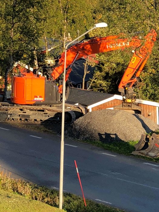 Stor orange Hitachi-grävmaskin vid arbetsplats för vägbygge med grushögar.