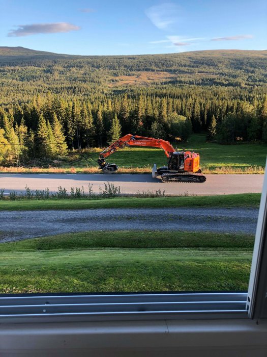 Stor orange grävmaskin redo att rivstarta bygget av ny väg med skogsbakgrund.