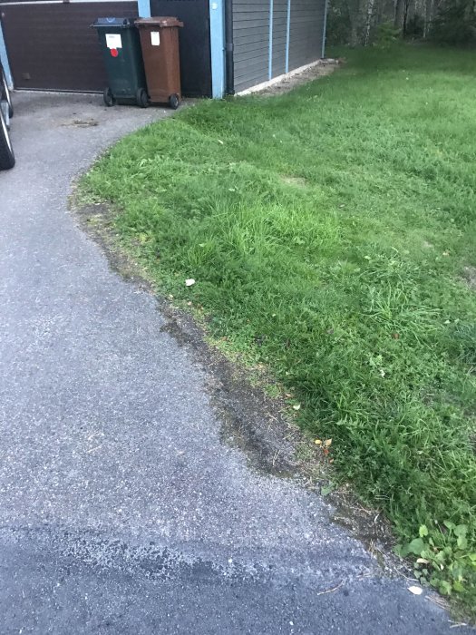 Gräsmatta och en asfalterad gångväg som leder mot ett garage, med potentiell yta för markstensläggning.