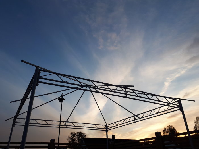 Metallram till en paviljong mot en himmel med solnedgång, ungefär 3x3 meter i storlek.