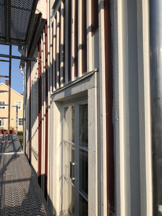 Nyrenoverad fasad på hus med målad plåt, tjockare vindskivor och en vit källardörr, sedd från en byggnadsställning.