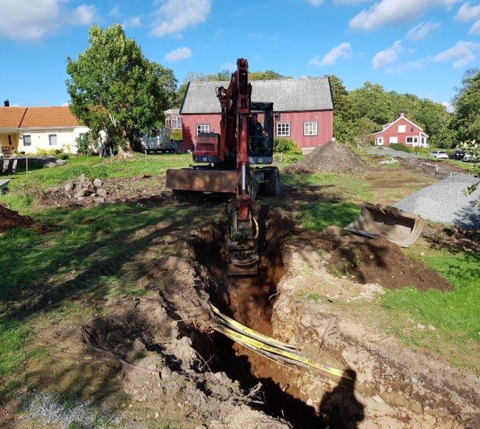 Grävmaskin gräver för avlopp i ett trädgårdsprojekt med omgivande hus och natur.