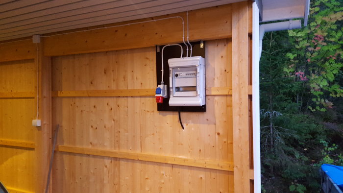 Nyinstallerad elcentral i carport med rörelsesensor och utomhuskabel på trävägg.