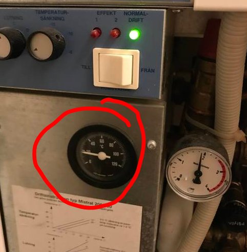 En termometer på en värmepanna som visar 20 grader, omgivet av andra kontrollenheter och ledningar.